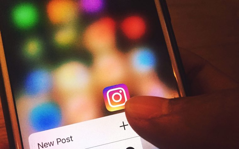 Finger navigating Instagram app on a smartphone screen with colorful blurred background. Un doigt naviguant sur l'application Instagram sur l'écran d'un smartphone avec un arrière-plan flou coloré.