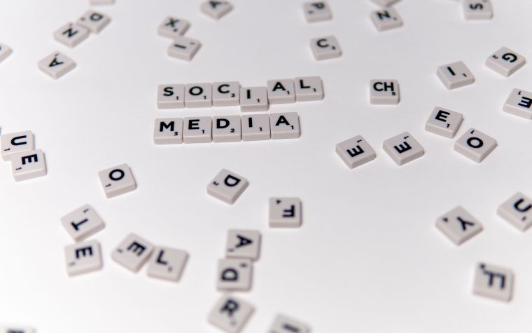 White Scrabble tiles forming the phrase 'social media' on a scattered background. Des tuiles Scrabble blanches formant la phrase « réseaux sociaux » sur un fond dispersé.