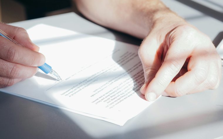 Hands signing a contract with a blue pen, close-up view. Des mains signant un contrat avec un stylo bleu, vue rapprochée.