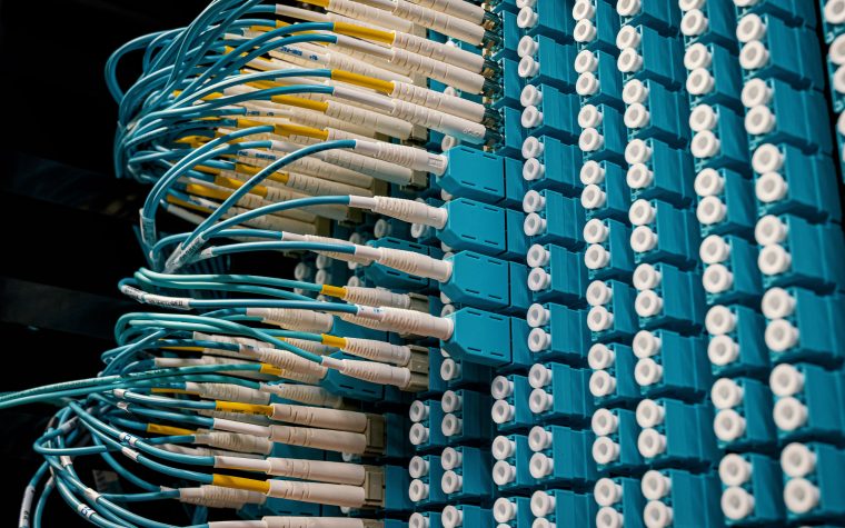 Detailed view of fiber optic patch cables connecting to a blue patch panel in a data center. Vue détaillée des câbles de brassage à fibre optique se connectant à un panneau de brassage bleu dans un centre de données.
