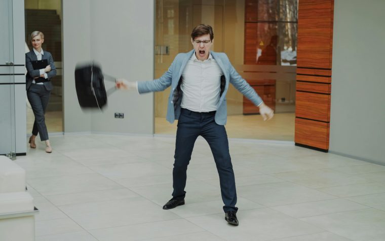 A businessman expresses frustration by throwing his briefcase inside a modern office setting. Un homme d'affaires exprime sa frustration en jetant sa mallette dans un cadre de bureau moderne.