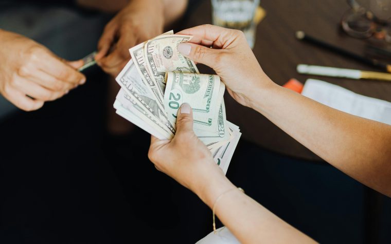 Close-up of hands counting cash in an indoor setting, conveying transaction theme. Gros plan sur des mains comptant de l'argent en espèces dans un cadre intérieur, véhiculant un thème de transaction.