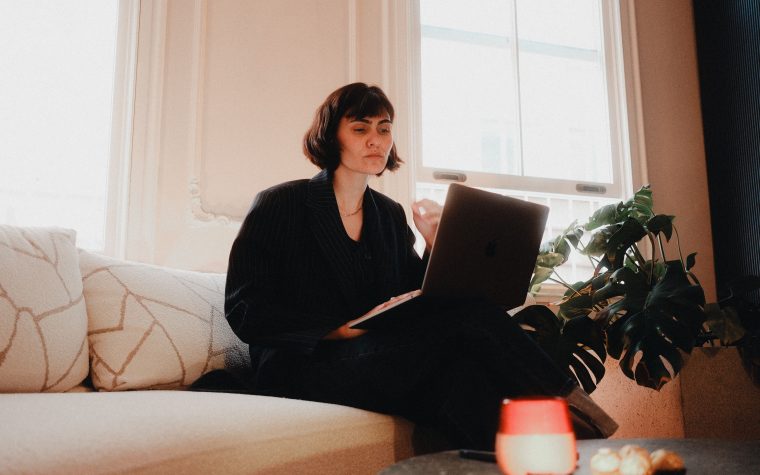 Woman in suit using laptop on sofa in bright room, modern lifestyle. Femme en costume utilisant un ordinateur portable sur un canapé dans une pièce lumineuse, mode de vie moderne.